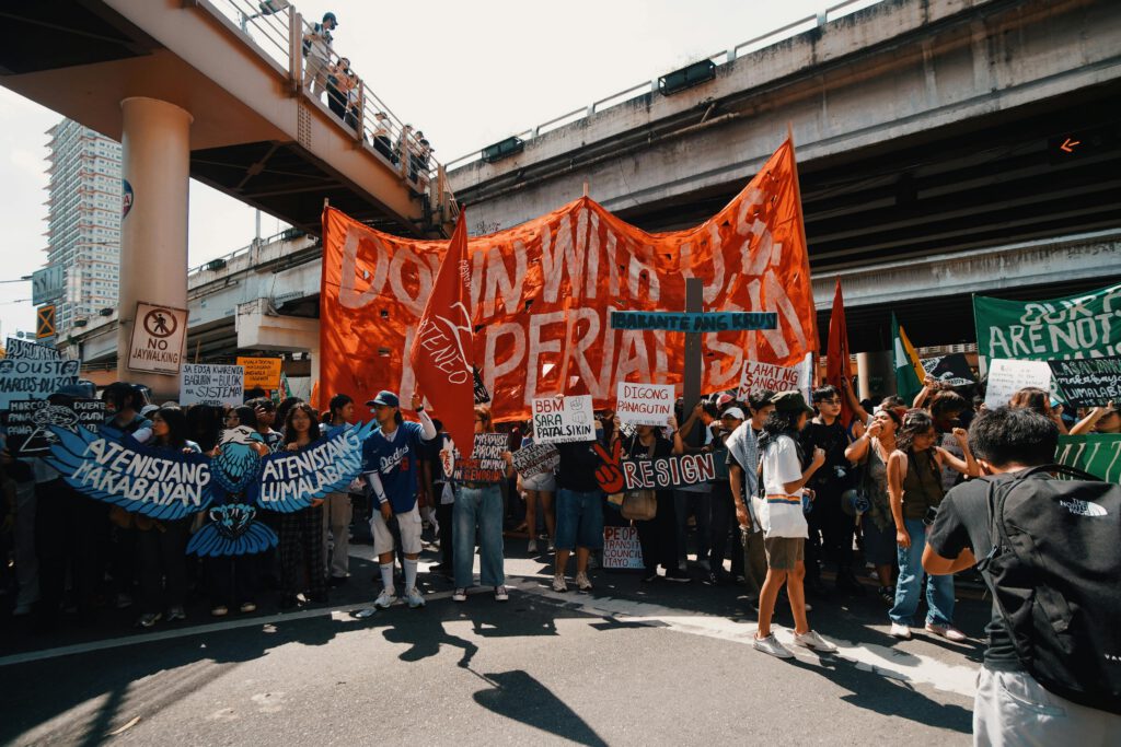 Crowd of protesters with banners under a city overpass during daytime.
